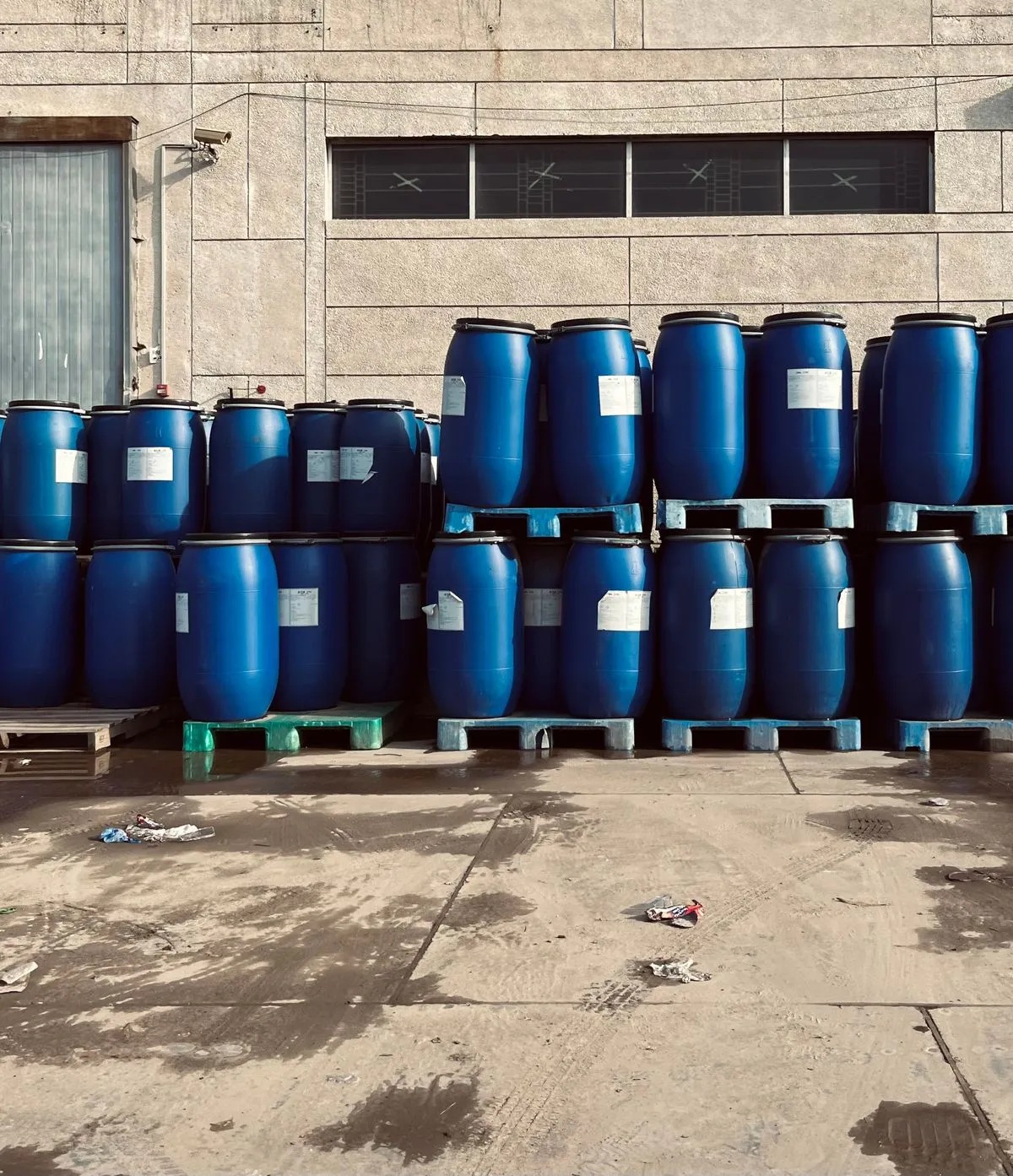 Blue industrial barrels stacked on pallets outside a warehouse